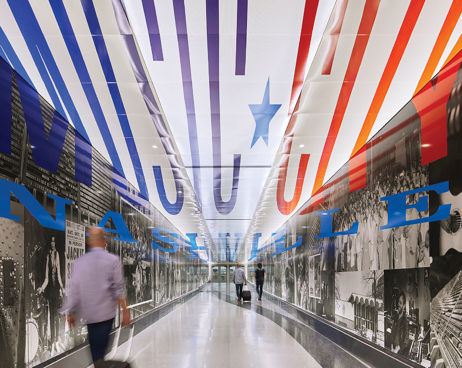 A man walking down a long hallway with colorful ceiling.