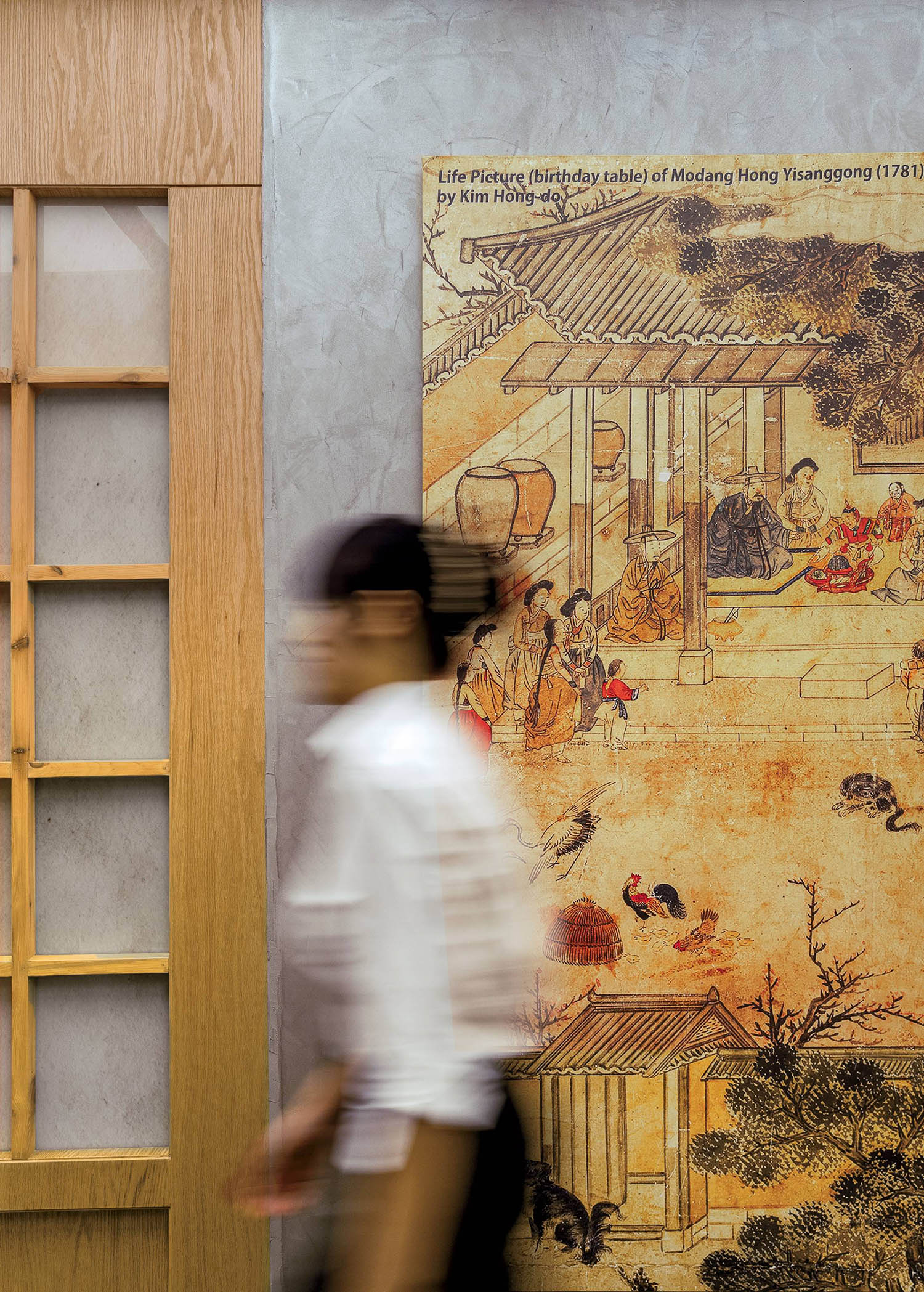 A man walking past a painting of a chinese village.